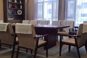 A conference room with a long table and chairs, a bookshelf with decorative items, and a view through the window. - Jinshan Hotel (Harqin Banner)