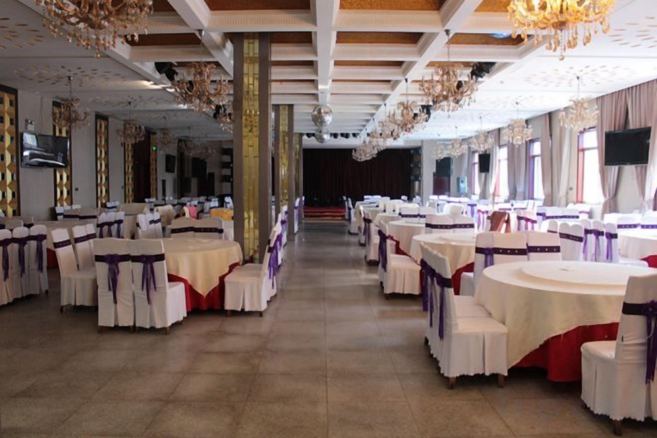 A banquet hall with round tables, chairs, and a stage.
