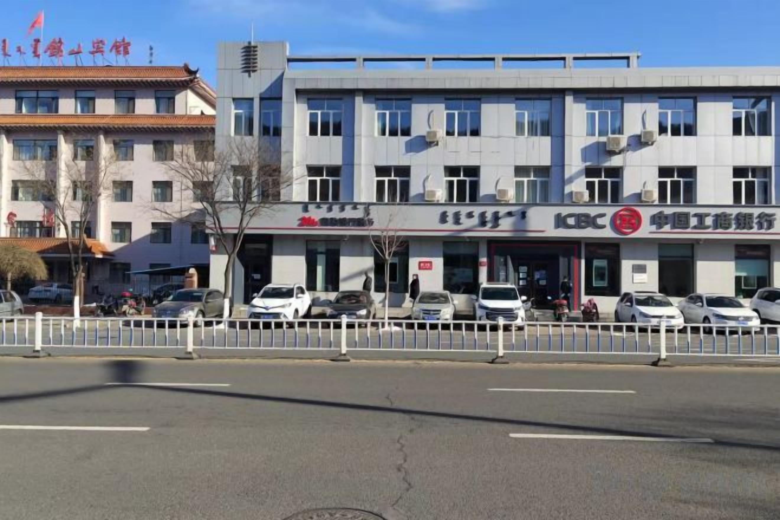 Un immeuble à plusieurs étages, doté d'une enseigne commerciale, d'un parking et d'une clôture blanche.