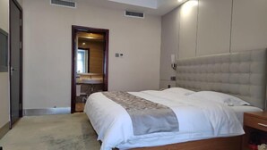A bedroom with a bed, a bedside table, a wardrobe, and a bathroom with a mirror. - Jinshan Hotel (Harqin Banner)