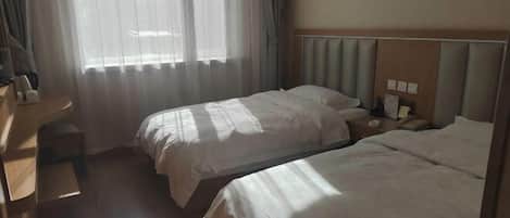 Ein Hotelzimmer mit zwei Betten, einem Schreibtisch und einem Fenster mit durchsichtigen Vorhängen.