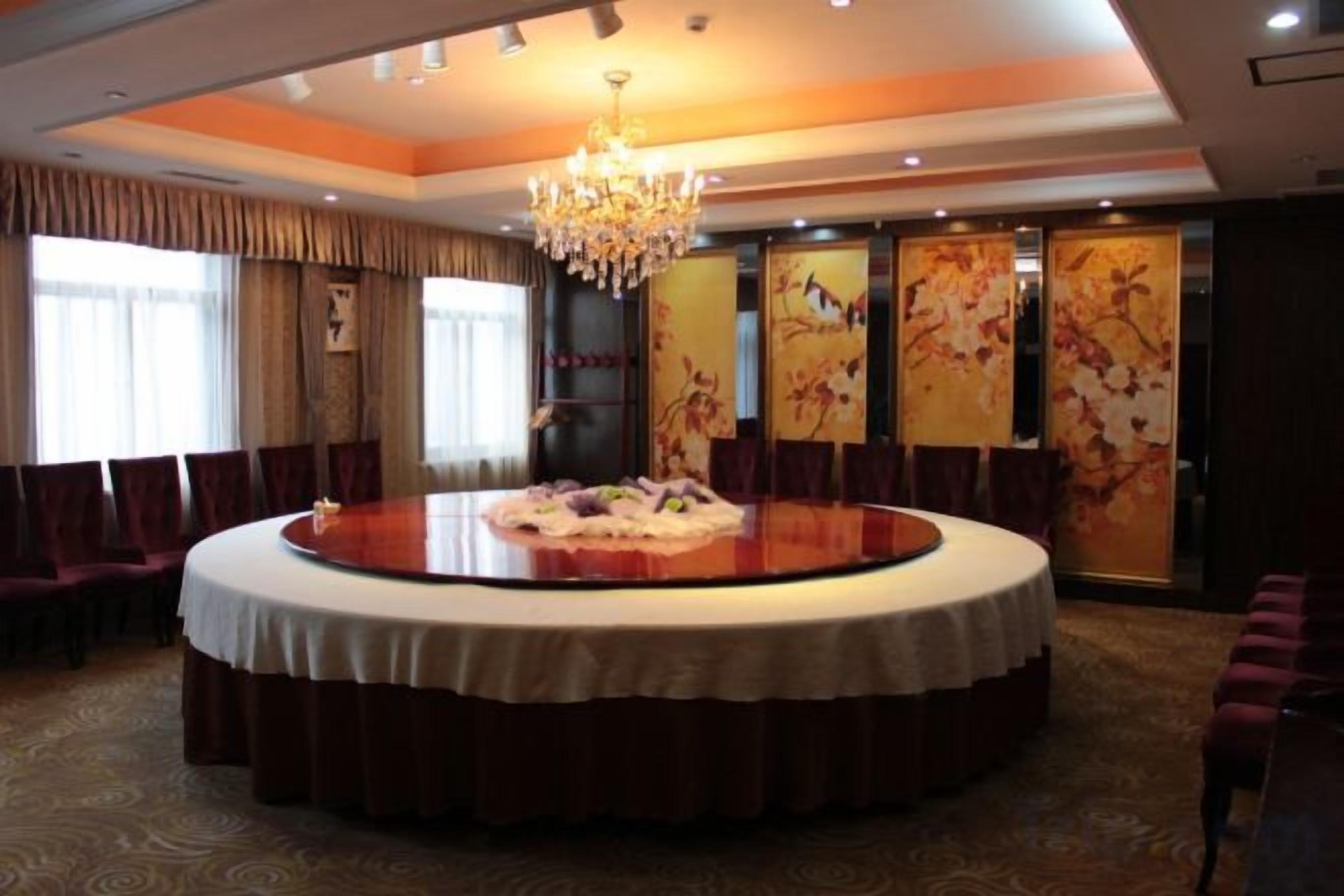 A round table with a white tablecloth in a room with a chandelier, curtains, and floral artwork on the walls.