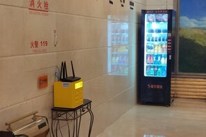 A vending machine with beverages, a fire alarm, and a yellow box on a cart. - Jinshan Hotel (Harqin Banner)