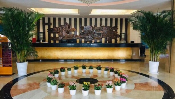 A lobby with a reception desk, a decorative wall, and a circular arrangement of potted plants. - Jinshan Hotel (Harqin Banner)