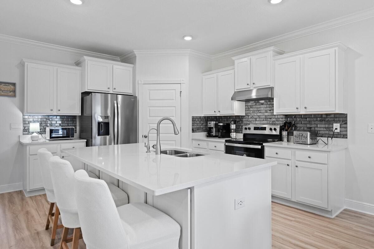 Una cocina moderna con armarios blancos, un refrigerador de acero inoxidable, un horno empotrado y una isla grande con asientos.
