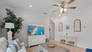 A modern living room with a white sofa, a coffee table, a TV on a white cabinet, a ceiling fan, and decorative wall panels. - 14 Beds | Sleeps 16 | Piper Cove Retreat | Pool | Santa Rosa Beach (Santa Rosa Beach)