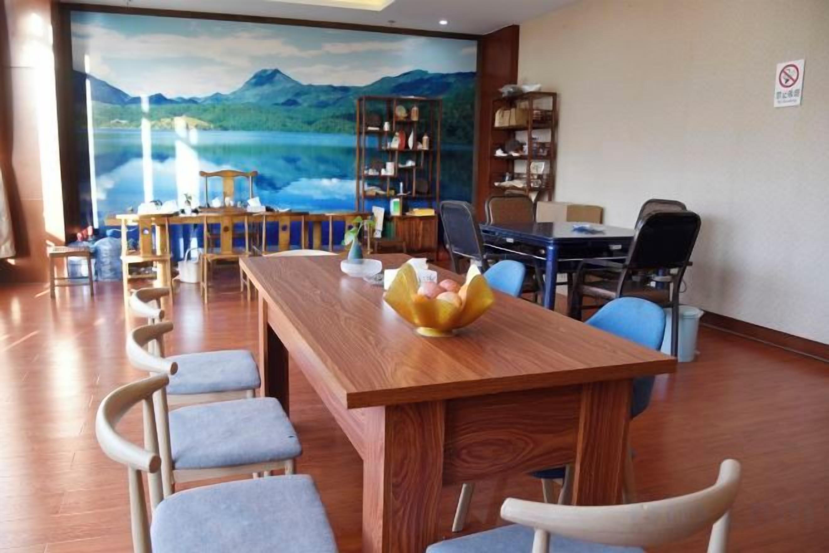 A dining area with a long wooden table, several chairs, and a view of a lake through a large window.