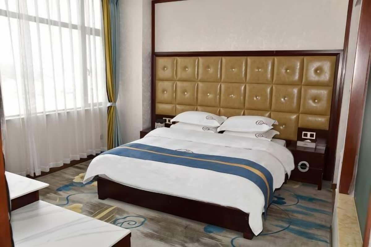 Una habitación de hotel con una cama grande, una mesita de noche y una ventana con cortinas.