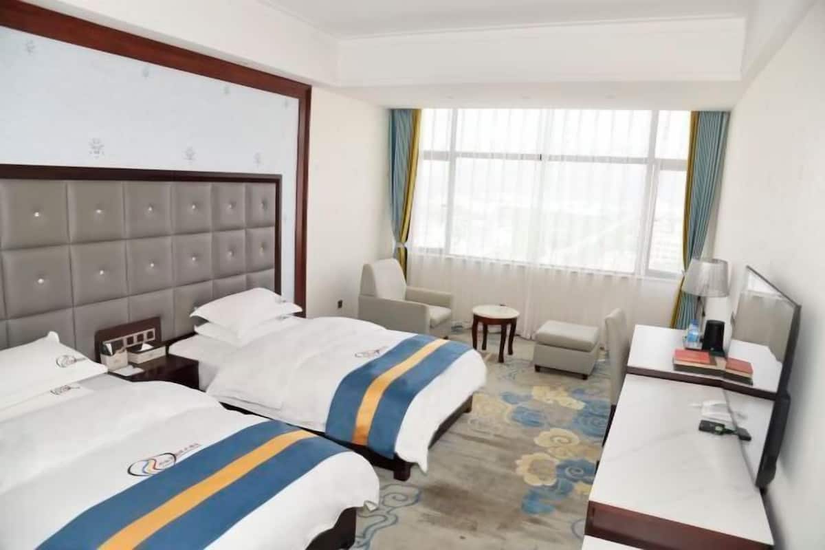 Habitación de hotel con dos camas, un sofá, una mesita y un escritorio con una lámpara.