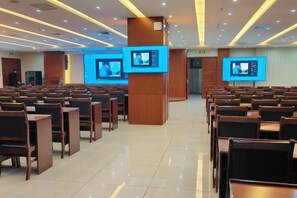 A conference room with rows of wooden chairs, two large screens, and a podium.