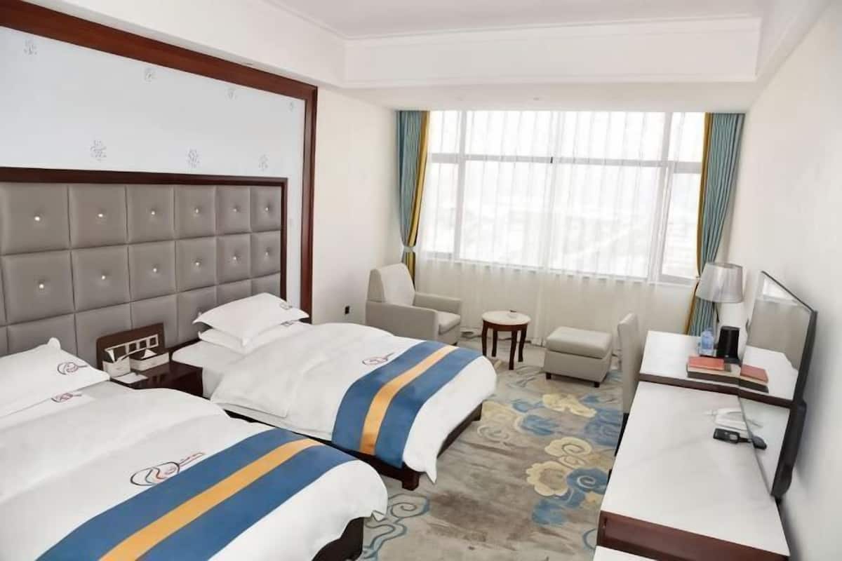 Habitación de hotel con dos camas, un escritorio, una silla, una mesita y una ventana con cortinas.