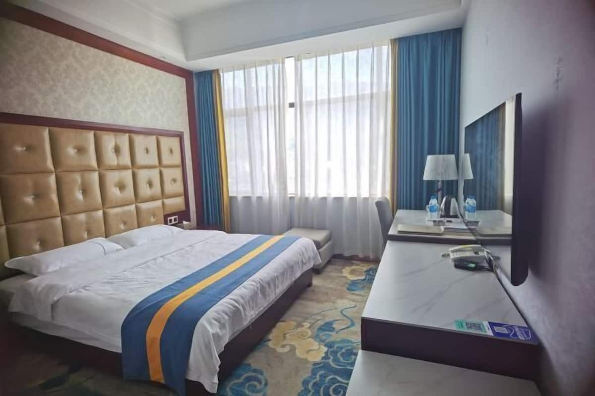 Habitación de hotel con una cama grande, un escritorio con lámpara, un espejo y una ventana con cortinas.
