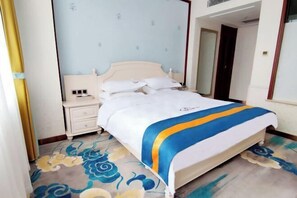 Una cama bien hecha con una colcha azul y blanca, una mesita de noche con una lámpara, y una alfombra estampada.