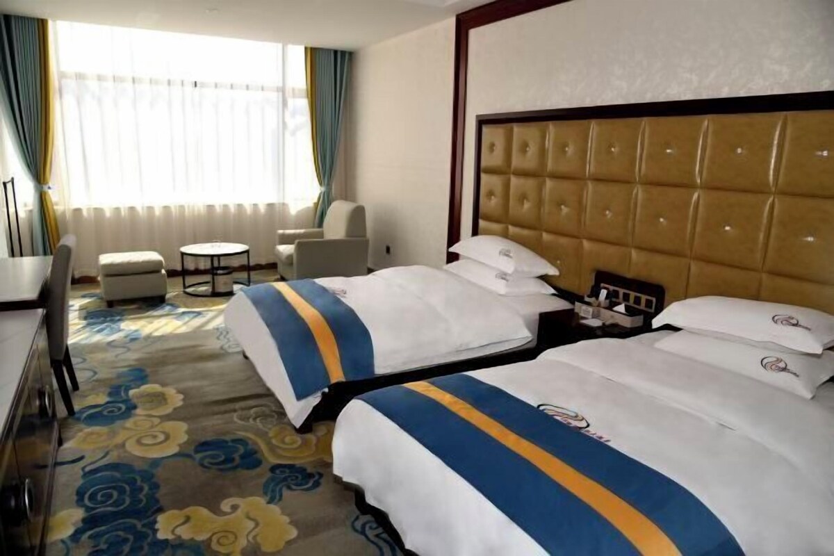 Una habitación de hotel con dos camas, un ventanal con cortinas, una mesa redonda y un sofá.
