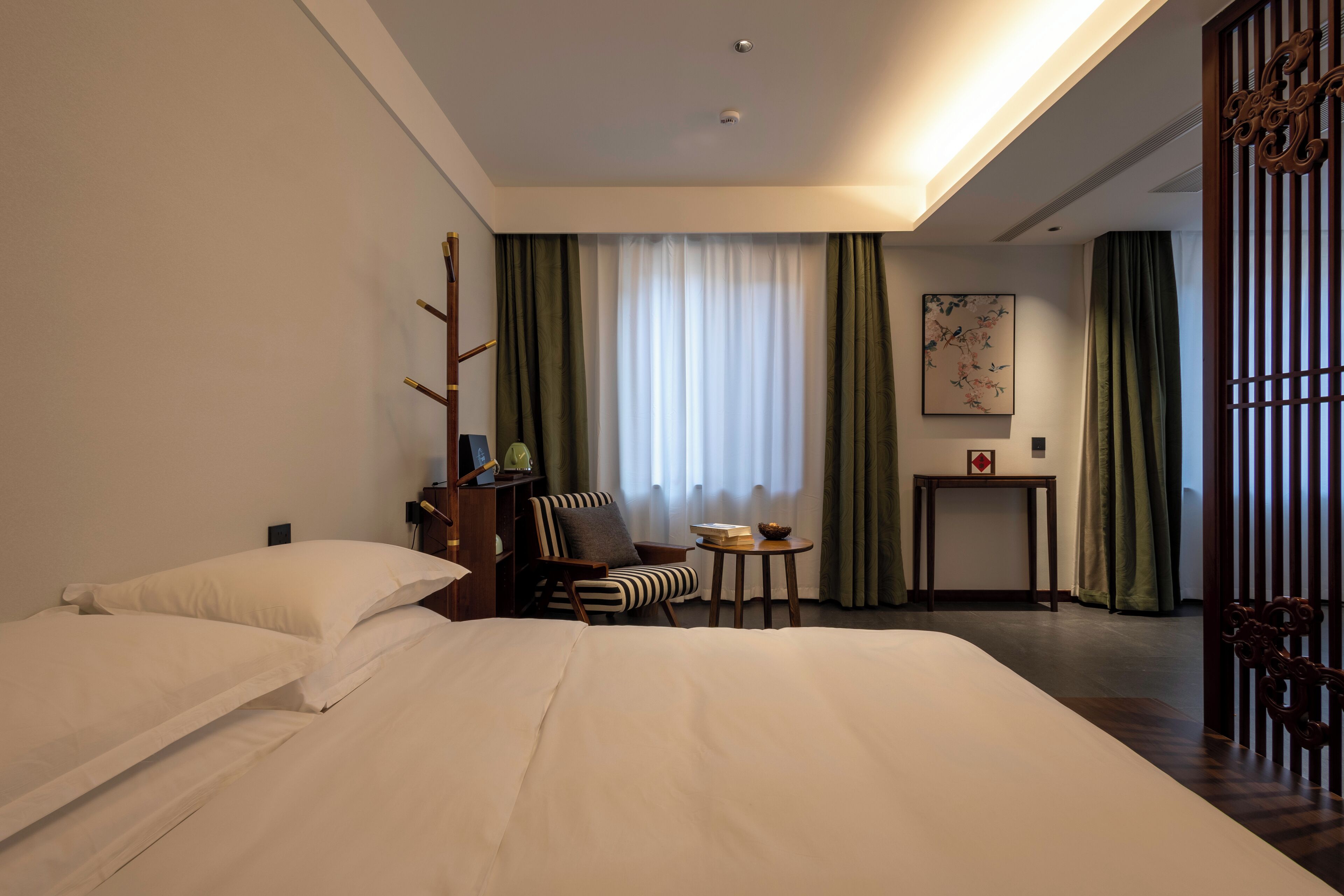 Una habitación de hotel con una cama grande, una silla, una mesita pequeña y un biombo decorativo.