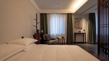 Una habitación de hotel con una cama grande, una silla, una mesita pequeña y un biombo decorativo.