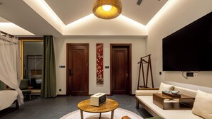 A modern hotel room with a sofa, a small table with a radio, a TV, and a bed with a canopy.