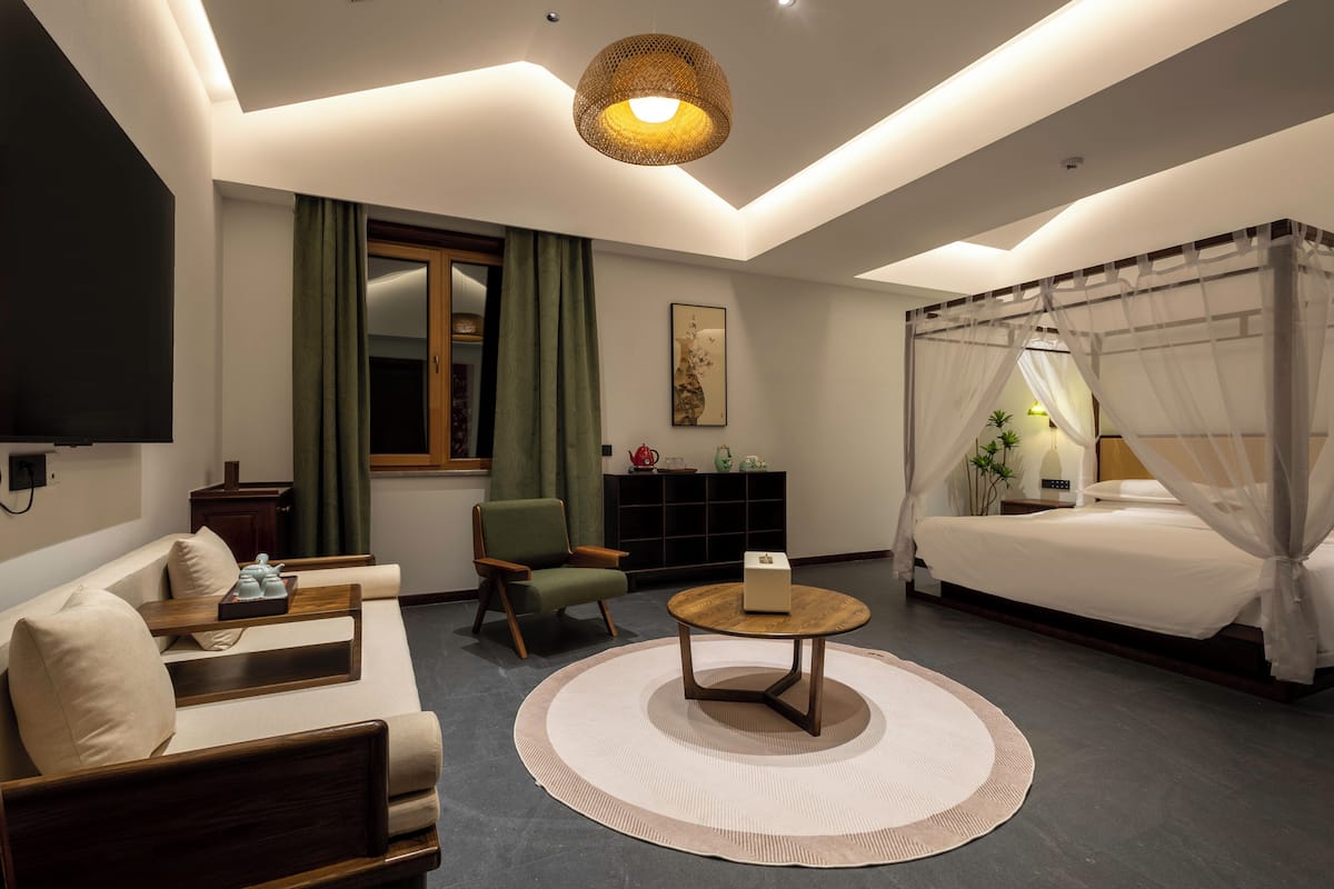 Une chambre moderne comprenant un lit, un canapé, un fauteuil, une table ronde et un téléviseur.