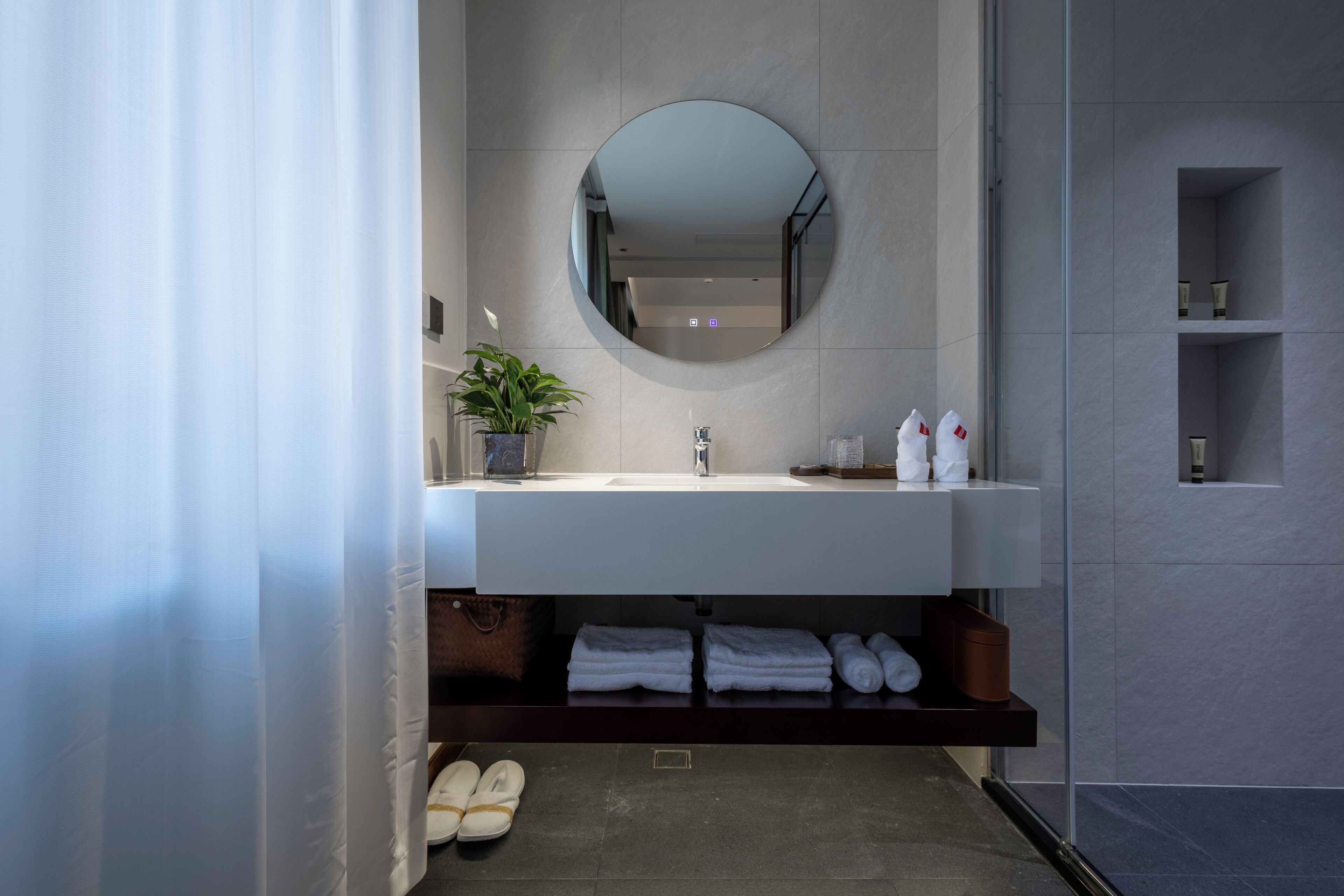 Un baño moderno con un espejo redondo, lavamanos blanco y estantes empotrados.