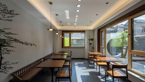 A modern interior with wooden tables and benches, large windows, and recessed ceiling lighting.
