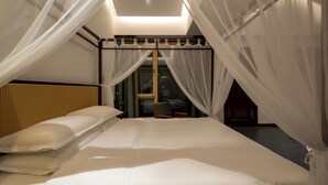A bedroom with a large bed, sheer curtains, and a view of the outdoors.