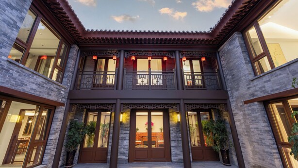 A traditional building with a courtyard, featuring a wooden balcony, large windows, and potted plants.
