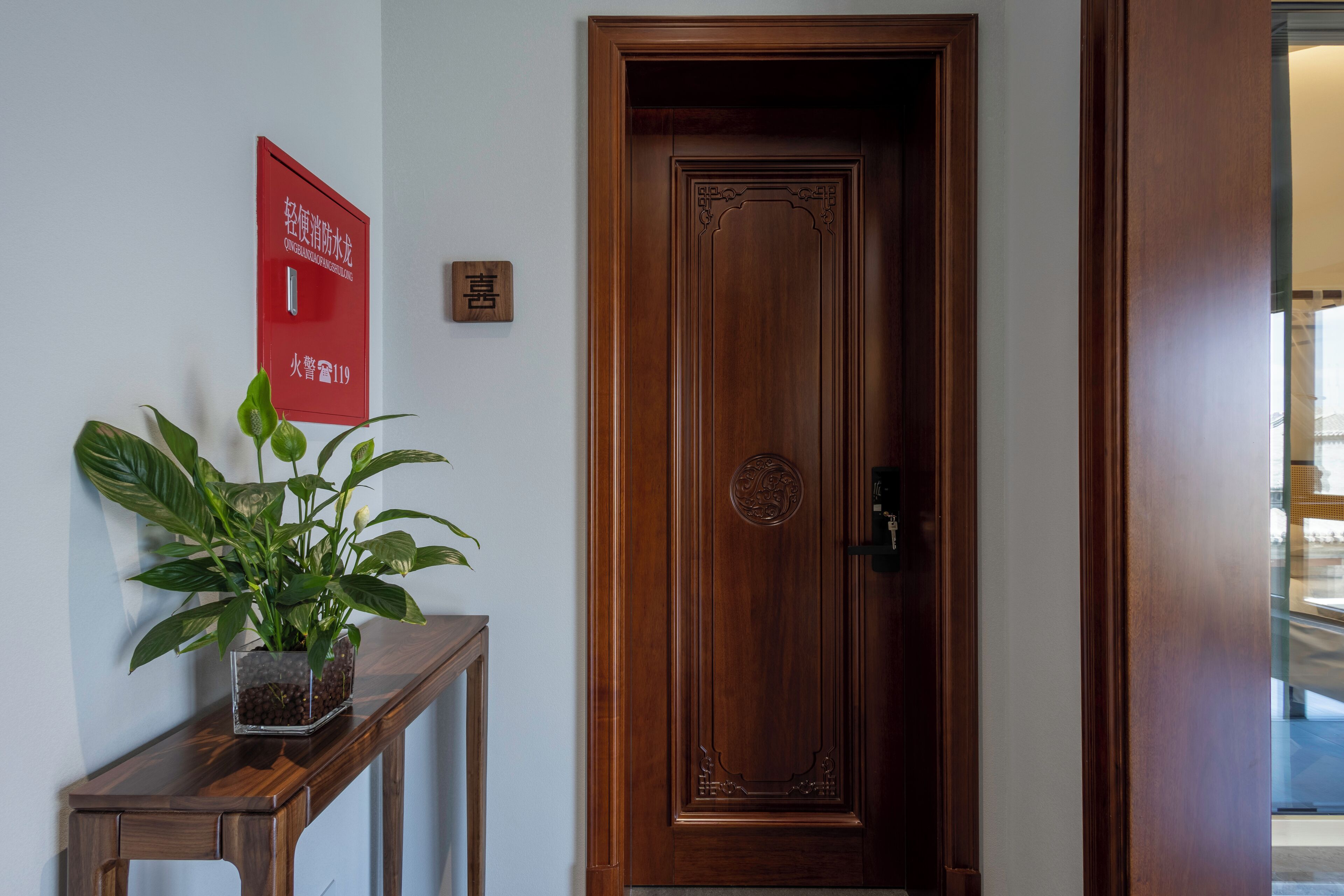 A wooden door with a decorative panel, a potted plant on a wooden console table, and a red sign with white text on the wall.