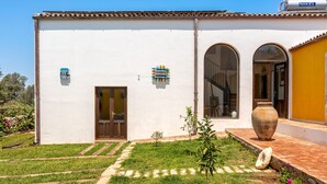 A building with a white facade, a yellow section on the right, and a large vase on the front porch.