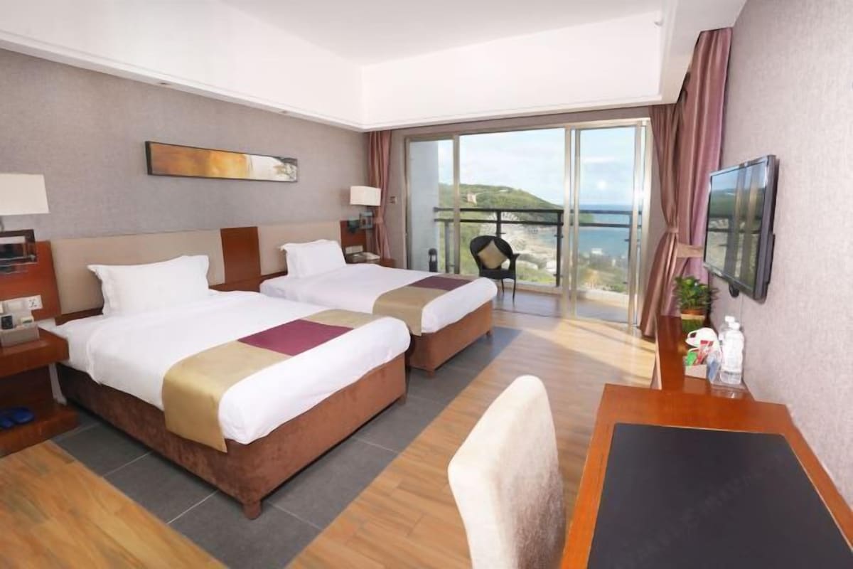 A hotel room with two beds, a balcony with a view, a desk, and a TV.