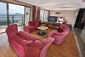 A modern living room with a large TV, red sofas, a coffee table, and a balcony with a view of the sea. - Galaxy Bay Hotel (Yangxi)