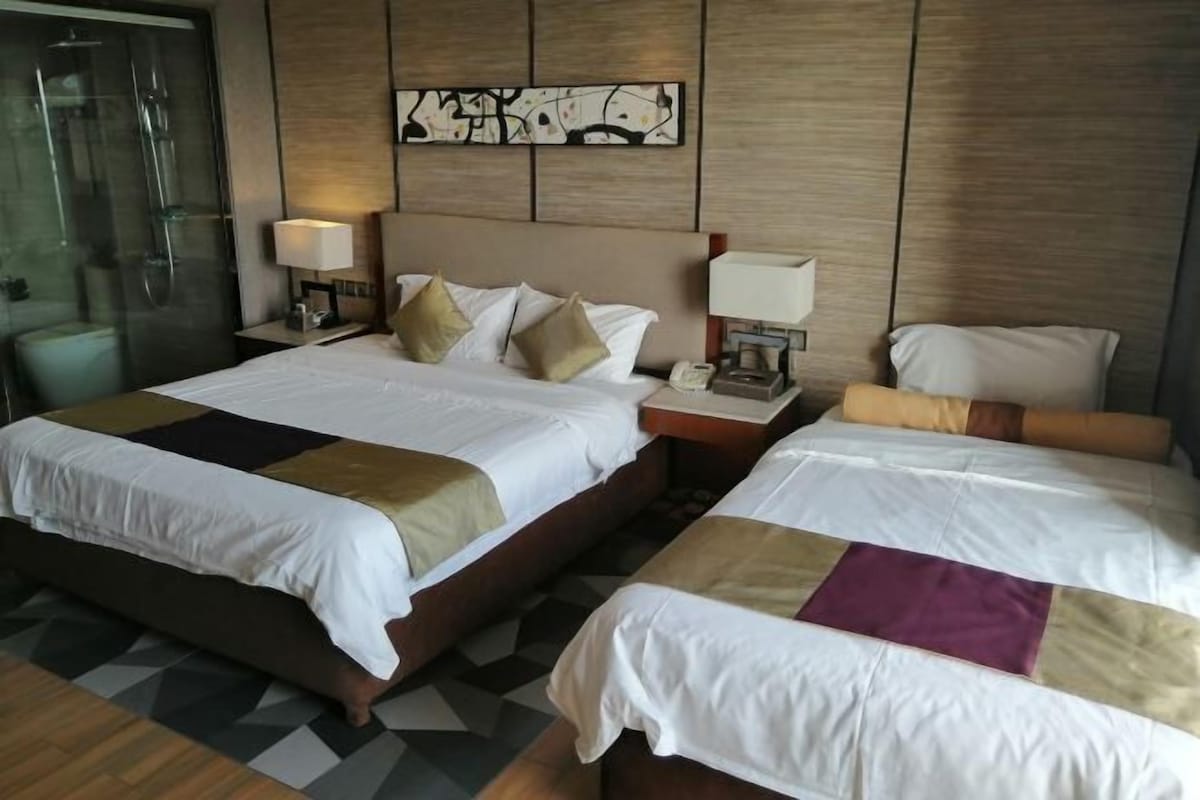 A hotel room with a large bed, two bedside tables, a headboard with artwork, and a shower area.