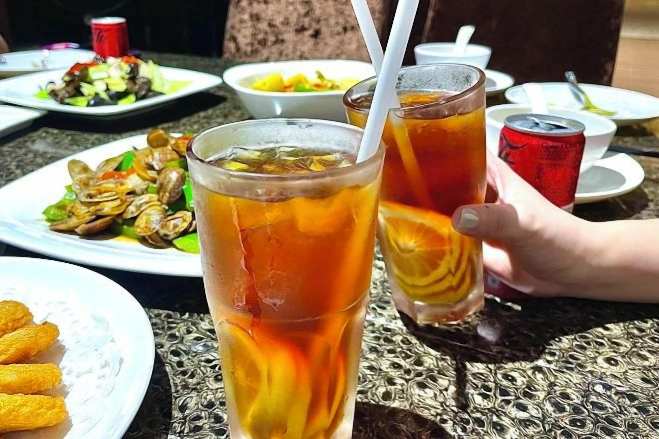 A table with food and drinks, including a plate of food, two glasses of iced tea, and a can of soda.