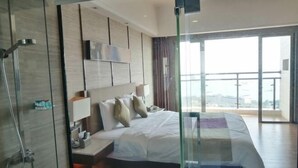 A modern hotel room with a large bed, a glass shower enclosure, a mounted TV, and a balcony with a city view. - Galaxy Bay Hotel (Yangxi)