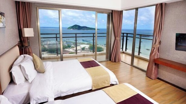A hotel room with a large bed, a TV, a window with a view of the sea and an island, and a balcony. - Galaxy Bay Hotel (Yangxi)