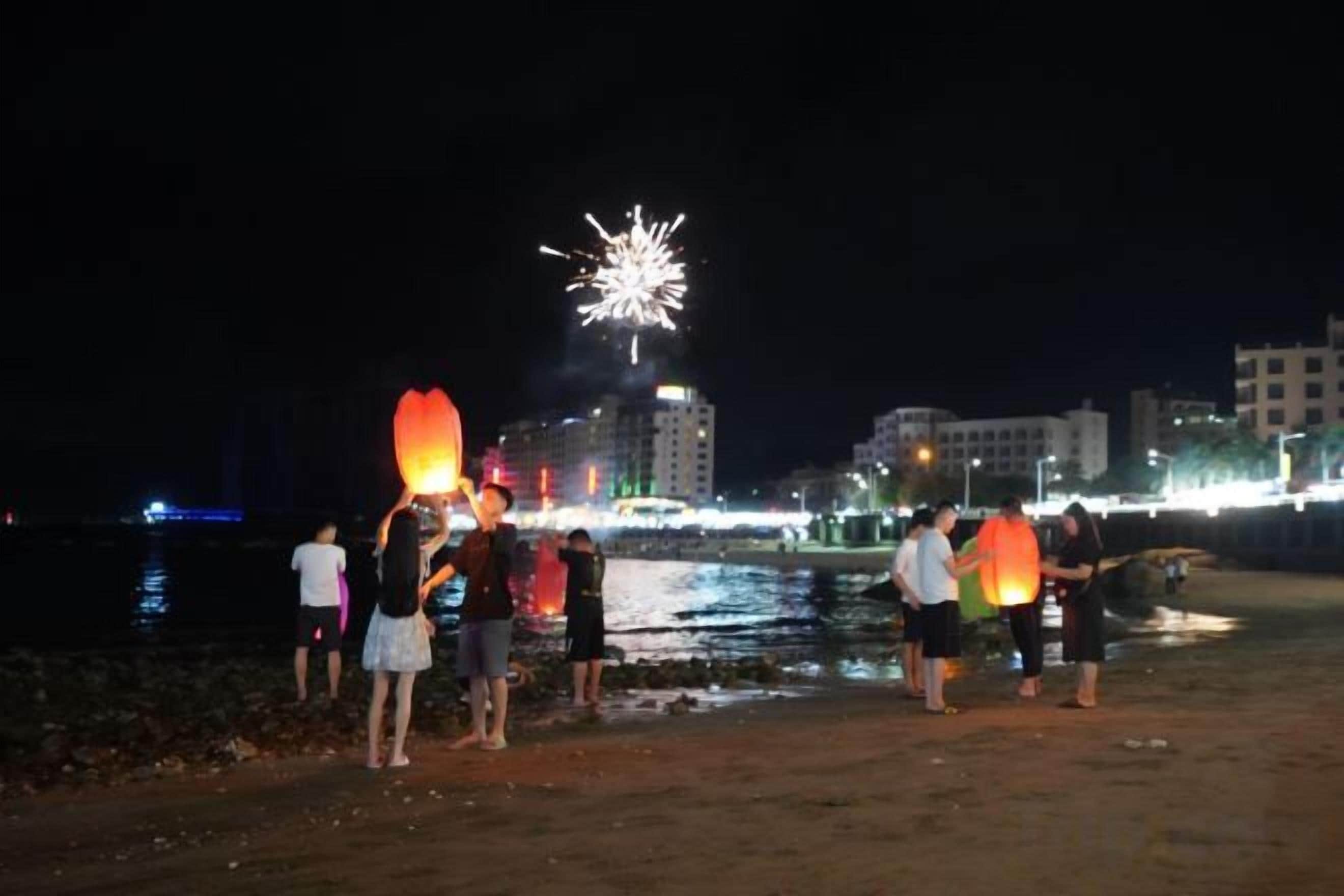 A group of people on a beach at night with fireworks in the background.
