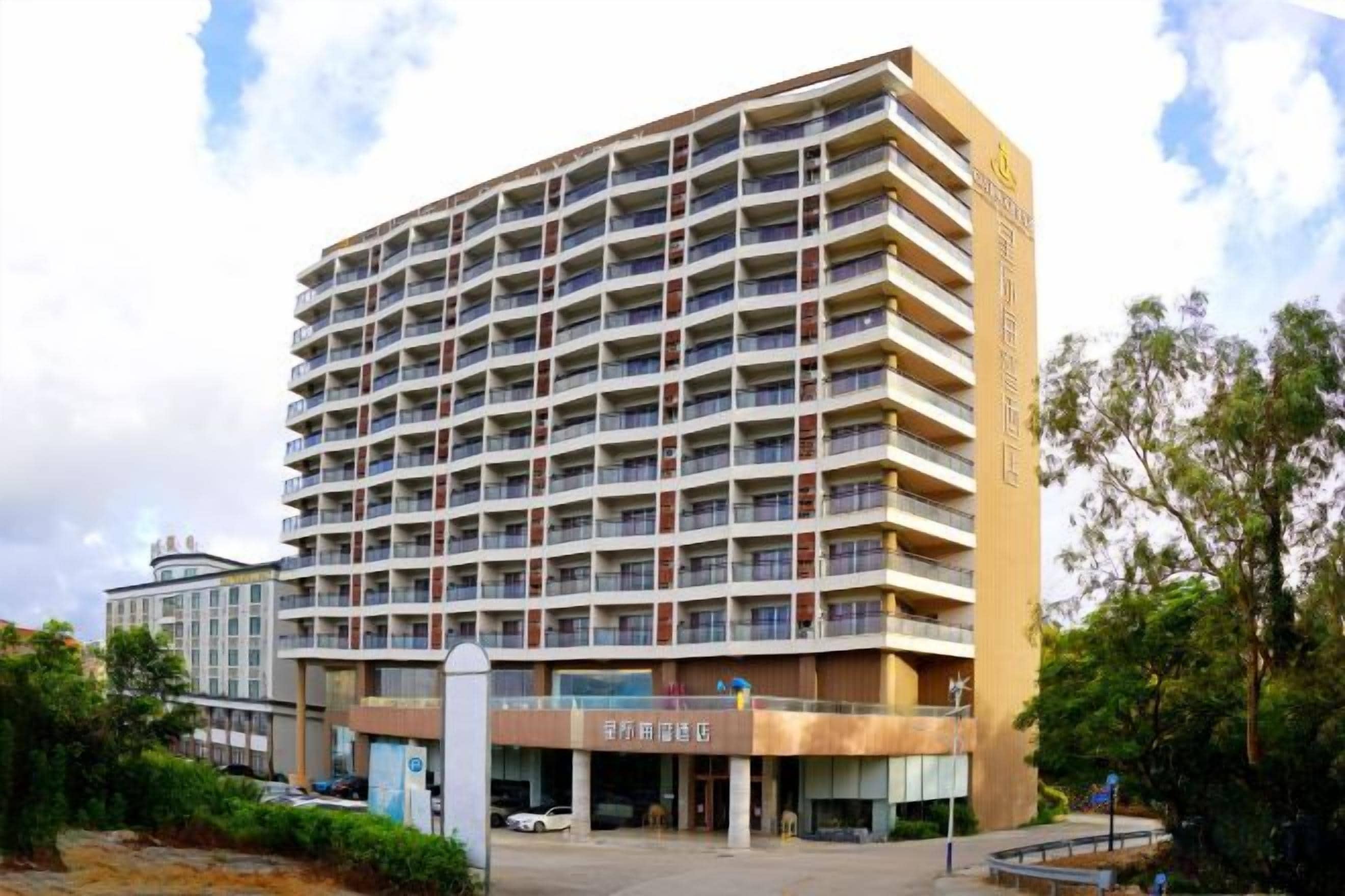 Un hôtel à plusieurs étages, doté d’une entrée centrale, de balcons à chaque étage et d’un espace de stationnement à l’avant.