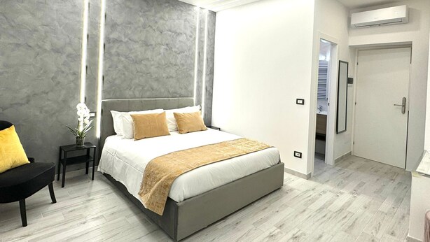 A modern bedroom with a large bed, bedside tables, a small side table with a plant, and a door leading to a bathroom. - Turati Inn (Rome)