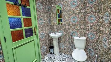 Une salle de bain avec une porte verte, un lavabo blanc et des toilettes. Les murs sont recouverts de carreaux à motifs.