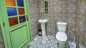 A bathroom with a green door, a white sink, and a toilet. The walls are covered with patterned tiles. - Ensuite Room in Tangier Medina

 (Tangier)