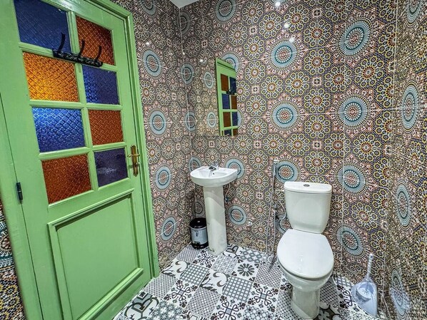 A bathroom with a green door, a white sink, and a toilet. The walls are covered with patterned tiles.