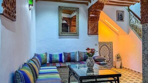 A Moroccan-style living room with a striped sofa, a glass coffee table, and a decorative mirror. - Ensuite Room in Tangier Medina

 (Tangier)