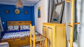 Une chambre avec un mur bleu, un lit en bois, une chaise en bois, une armoire et un miroir.