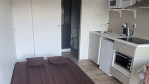 Habitación compacta con cama, kitchenette y puerta que da a otra habitación.