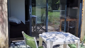 Una habitación con una puerta corrediza de vidrio que da a un patio. Hay una cama con cabecera blanca y una pequeña mesa con mantel blanco.