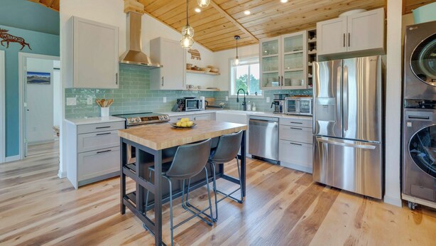 Una cocina moderna con vigas de madera, electrodomésticos de acero inoxidable y una isla central con sillas.