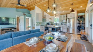 Una cocina amplia con electrodomésticos modernos, un comedor con una mesa de madera dispuesta para cuatro personas, y un sofá azul en la sala.
