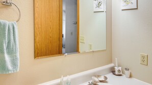 Un baño con puerta de madera, un espejo, toallero, lavabo y un portalápices para cepillos de dientes.