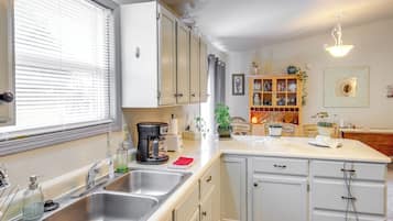 A kitchen with white cabinets, a double sink, a coffee maker, and a window with blinds.