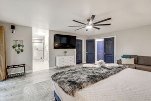 Une chambre à coucher avec un lit, un ventilateur de plafond, une télévision et une grande fenêtre.