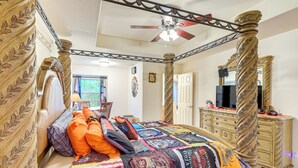 Un letto a baldacchino con una coperta trapuntata, una ventola a soffitto e un comò in legno con uno specchio.